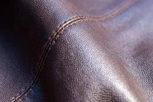 Close-up of smooth, soft brown lambskin leather texture with visible stitching detail.