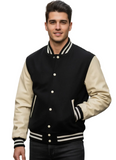 A man wearing a classic varsity jacket with black wool body and cream-colored sleeves, standing in an outdoor urban setting with a blurred background.