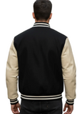 A man viewed from behind wearing a black and cream varsity jacket on a blurred city street background.