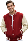 A smiling young man wearing a classic varsity jacket with a deep red body and cream-colored sleeves, standing outdoors with a blurred brick building in the background.